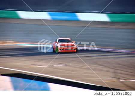 ドリフトするオレンジ色のセダン車 135581806