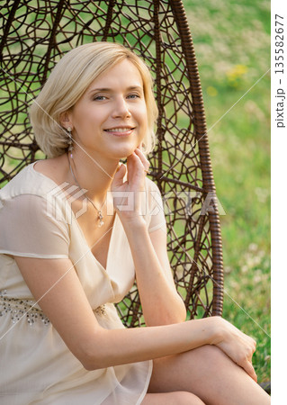 Woman sits in a hanging chair outside with a smile on her face during the afternoon light Woman sits in a hanging chair outside with a smile on her face during the afternoon light 135582677