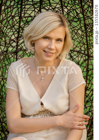 Woman sitting in a woven chair in a garden during sunny weather Woman sitting in a woven chair in a garden during sunny weather 135582678