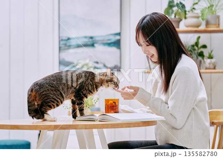 リビングのテーブルで猫とくつろぐ若い女性 リビングのテーブルで猫とくつろぐ若い女性 135582780