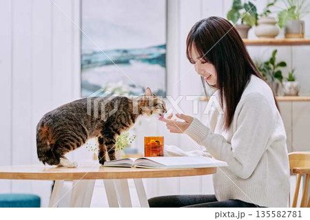 リビングのテーブルで猫とくつろぐ若い女性 135582781