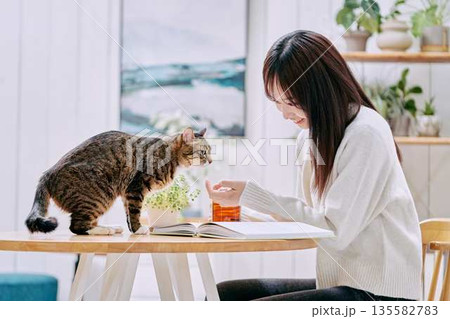 リビングのテーブルで猫とくつろぐ若い女性 135582783