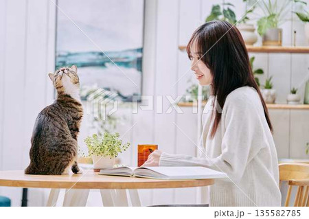 リビングのテーブルで猫とくつろぐ若い女性 135582785