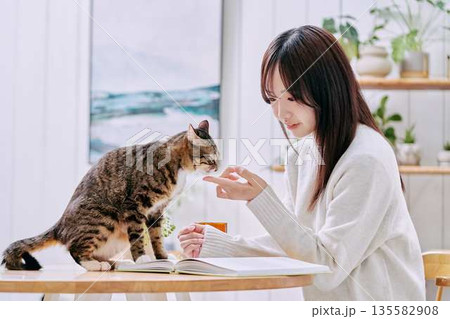 リビングのテーブルで猫とくつろぐ若い女性 135582908