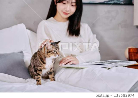 ベッドの上で猫とリラックスして本を読む女性 ベッドの上で猫とリラックスして本を読む女性 135582974