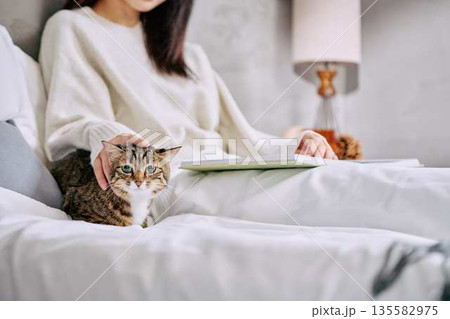 ベッドの上で猫とリラックスして本を読む女性 ベッドの上で猫とリラックスして本を読む女性 135582975