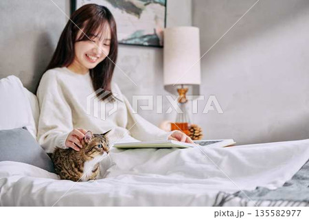 ベッドの上で猫とリラックスして本を読む女性 135582977