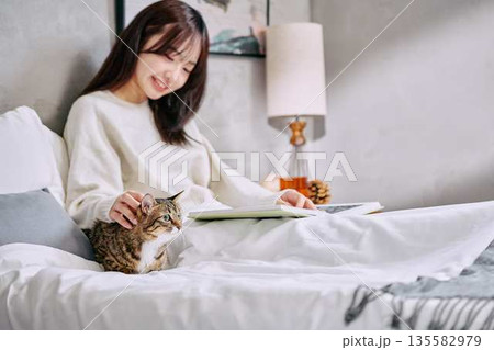 ベッドの上で猫とリラックスして本を読む女性 135582979