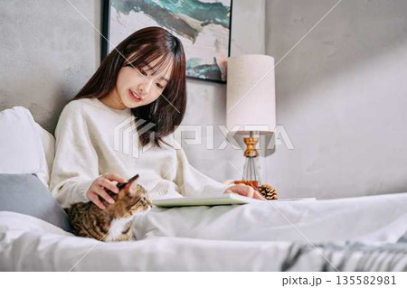 ベッドの上で猫とリラックスして本を読む女性 ベッドの上で猫とリラックスして本を読む女性 135582981