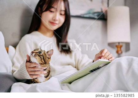 ベッドの上で猫とリラックスして本を読む女性 135582985