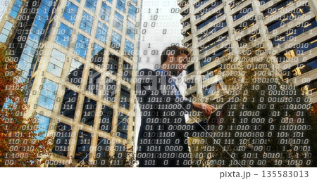 Male wearing dark suit holding phone engaging with data streams in city street, amid office towers 135583013