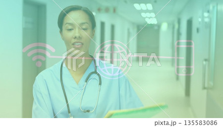 Standing nurse in scrubs, holding folder with stethoscope in hospital corridor, with digital icons Standing nurse in scrubs, holding folder with stethoscope in hospital corridor, with digital icons 135583086