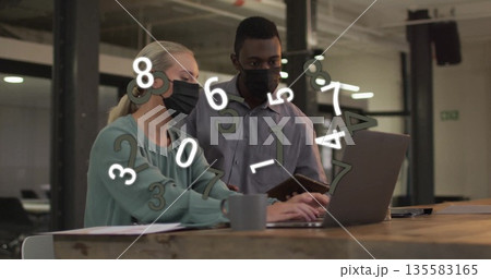 Working masked coworkers analyzing data in open office with laptop, tablet, coffee mug papers Working masked coworkers analyzing data in open office with laptop, tablet, coffee mug papers 135583165