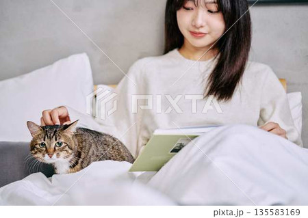 ベッドの上で猫とリラックスして本を読む女性 135583169