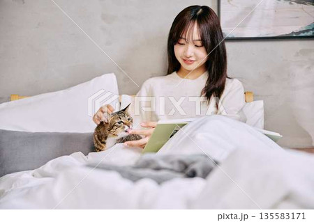 ベッドの上で猫とリラックスして本を読む女性 ベッドの上で猫とリラックスして本を読む女性 135583171