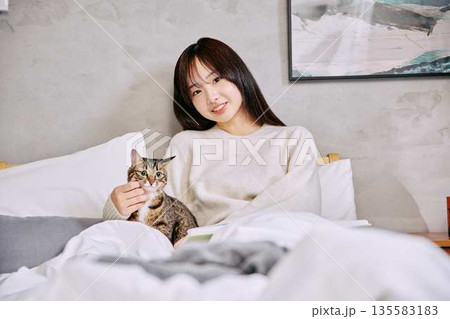 ベッドの上で猫とリラックスして本を読む女性 135583183