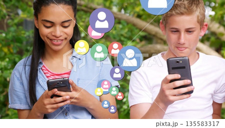 Browsing friends in casual clothes with smartphones under leafy tree, avatar icons floating around 135583317
