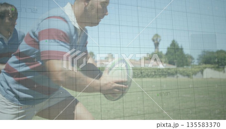 Charging rugby player in striped jersey gripping rugby ball and driving forward on suburban field 135583370