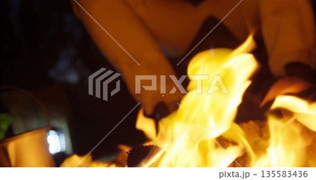 Crackling flames roaring around logs in outdoor fire pit, with boots and pants above 135583436