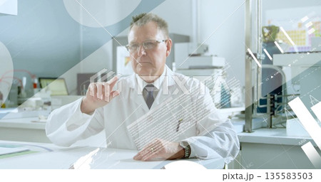 Senior scientist wearing lab coat and tie using data overlays at lab bench, with glassware Senior scientist wearing lab coat and tie using data overlays at lab bench, with glassware 135583503