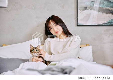 ベッドの上で猫とリラックスして本を読む女性 135583518