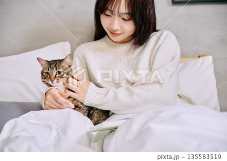 ベッドの上で猫とリラックスして本を読む女性 135583519
