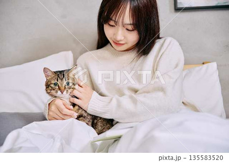 ベッドの上で猫とリラックスして本を読む女性 ベッドの上で猫とリラックスして本を読む女性 135583520