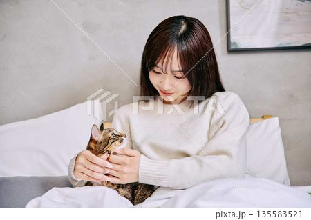 ベッドの上で猫とリラックスして本を読む女性 135583521