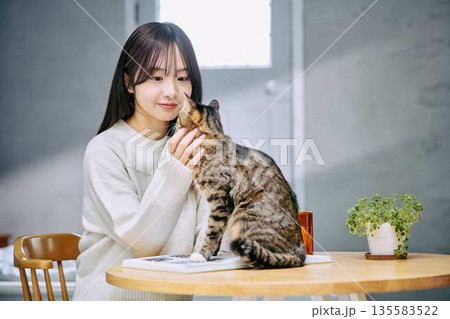 テーブルの上で猫を撫でて愛でる女性 135583522