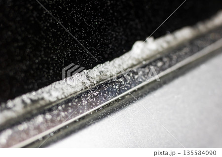 Ice and snow on windshield, Driver clears icy frost from windshield with scattered particles 135584090