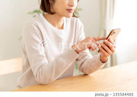 部屋でスマホを見るミドル女性 135584485