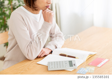 家計簿をつけながら悩むミドル女性 家計簿をつけながら悩むミドル女性 135585101