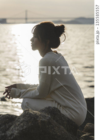 夕暮れの海を散策する女性 135585557
