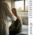 Doctor comforting elderly male patient in hospital room with empathetic care. 135585928