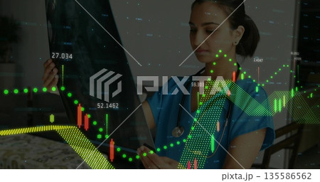 Doctor in scrubs studying radiograph film in office, with stethoscope digital financial charts 135586562