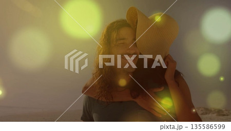 Carrying woman on back, bearded man strolling on sandy shoreline at sunset, with straw sunhat 135586599