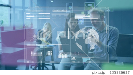 Two coworkers viewing laptop charts and data view in open-plan office with sticky note board 135586637