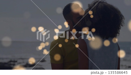 Kissing couple wearing summer attire on sandy shore, with ocean waves horizon line and bokeh lights 135586645