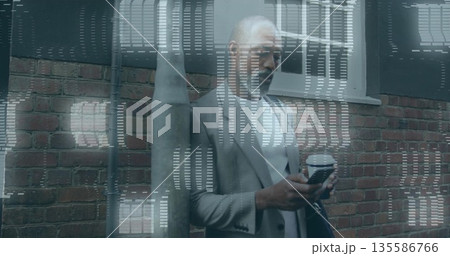 Leaning senior executive wearing suit checking smartphone on city sidewalk, with coffee cup and bag Leaning senior executive wearing suit checking smartphone on city sidewalk, with coffee cup and bag 135586766