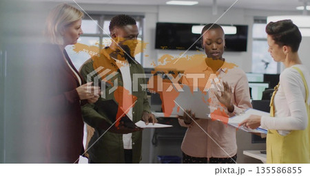 Collaborating team in business wear reviewing laptop and documents around map overlay in office Collaborating team in business wear reviewing laptop and documents around map overlay in office 135586855