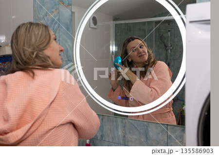 Woman Brushing Her Hair in a Bathroom Mirror in the Morning Light 135586903
