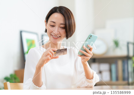 リビングでスマホとクレジットカードを見るミドルの女性 リビングでスマホとクレジットカードを見るミドルの女性 135586999