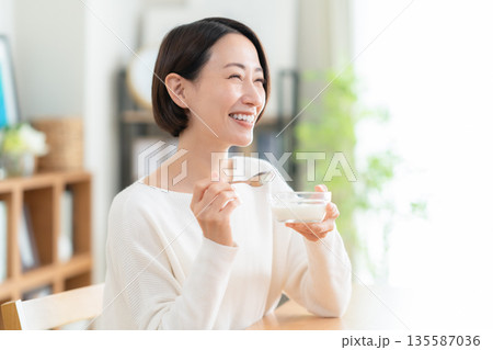リビングでヨーグルトを食べるミドルの女性 リビングでヨーグルトを食べるミドルの女性 135587036