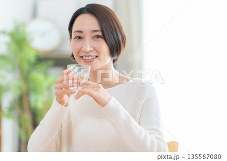 家でリビングで水を飲むミドルの女性 135587080