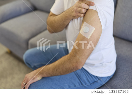 Man adjusting arm patch with glucose monitor sensor for wearable diabetes care 135587163