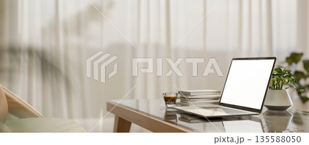 White screen laptop and coffee on glass top wooden table aside sheer curtain in a modern living room 135588050