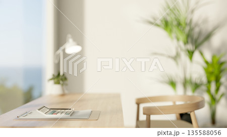 A calculator on clipboard with pencil and lamp on wooden table and chair beside glass window wall. 135588056