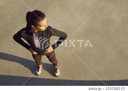 Young female runner resting after workout, hands on hips in warm sunlight 135588133