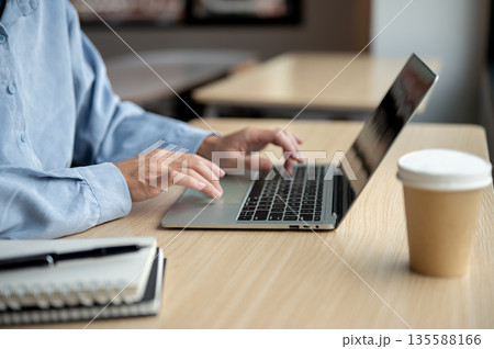 Close up man's hands typing on laptop aside books and coffee while sitting at wooden table in a cafe Close up man's hands typing on laptop aside books and coffee while sitting at wooden table in a cafe 135588166