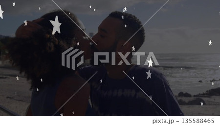 Kissing couple leaning close on sandy shoreline by railing with ocean waves, star-shaped overlays 135588465